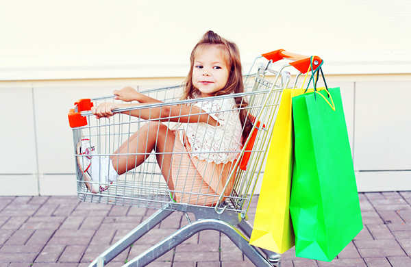 Happy smiling child sitting in trolley cart with colorful shopping bags having fun